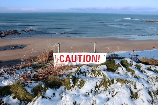 a red caution sign on a cliff edge in snow covered ballybunion