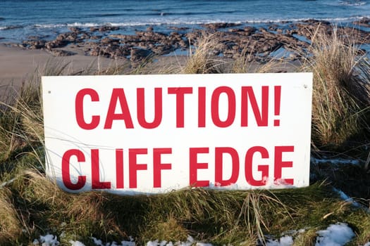 a red caution sign on a cliff edge in snow covered ballybunion