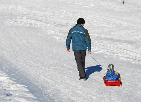 The father is sledding his sun in the Alpes