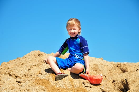 boy  wearing surf suit sitting in sand on the beach