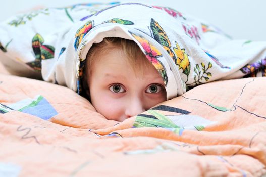 little boy laying under the pillow and watching something frightful on TV