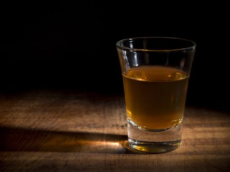 A single shot of an aged liquor over a wooden table.