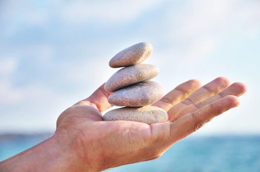 balancing stones in man's palm over blue sky
