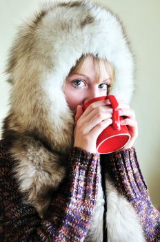 Girl in fur cap drinking tea from red cup

