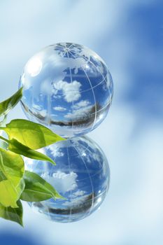 Closeup of glass globe and green leaves lying on mirror background with blue sky and clouds reverberation