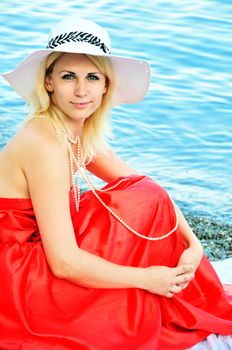 lady wearing red dress and straw hat and pearls on the beach
