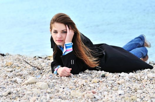 lovely teen girl laying on the pebble close to sea in spring time