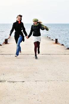 two happy running girls on the dock near the sea