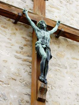 Green sculpture of Jesus on a wood cross on a wall