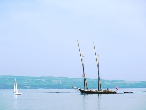 Big ancient boat and small white sailing boat on lake of Geneva, Switzerland, with little hill behind