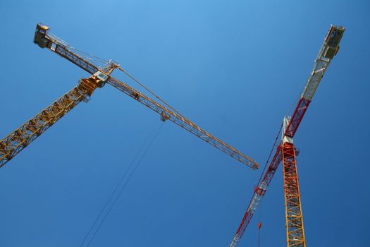 Two building cranes against cloudless sky