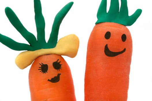 Close up of two carrots with smiling faces against a white background.