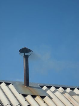 A smoking pipe on a roof on a background of the blue sky   