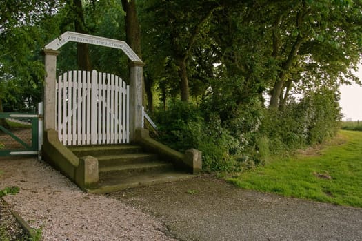 The phrase Ashes to Ashes and Dust to Dust is written in Dutch over the entrance of this cemetry. The scene lies peacefully in the evening light