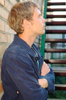 Young stylish man with blonde hair stand near brick wall and stairs.