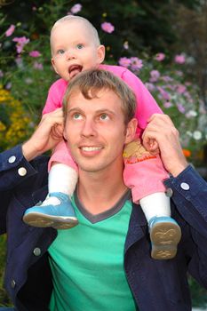 Proud father with his happy daughter sit on father's shoulders on flowers background.