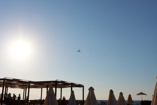 The aircraft in the sky. Relax at sea. People in the cafe on the shore.