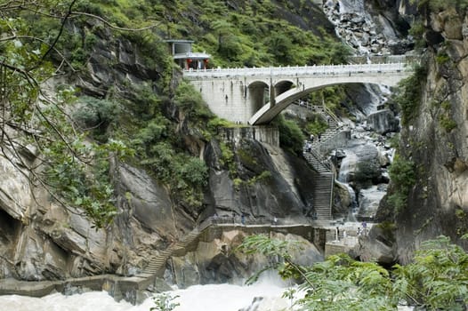 Sino-Tibetan mountains in Yunnan province, near Lijiang city, China. Bridge in ancient Chinese style over river.