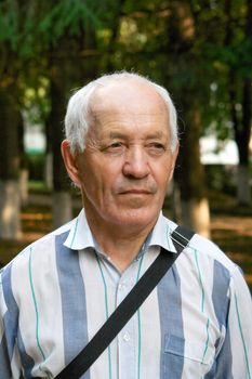 Portrait of the elderly man in a striped shirt against the nature