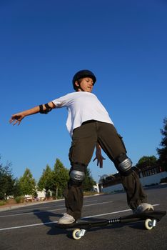 Boy balancing the skateboard shown against the blue sky