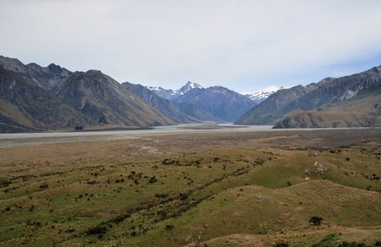 Mount Cook in New Zealand surrounded by clouds over a grassy plain