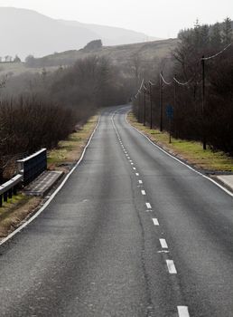 A single carriageway road leads into the distance among hills and meadows