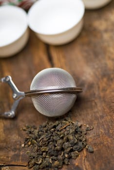 dry green chinese tea set,with strainer closeup,cups and teapot on background over old wood board