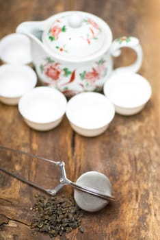 dry green chinese tea set,with strainer closeup,cups and teapot on background over old wood board