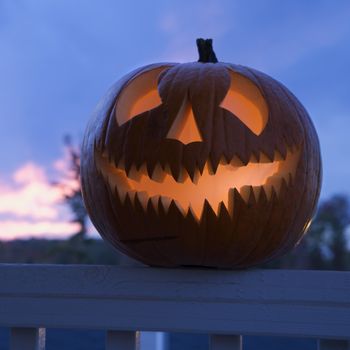 Carved Halloween pumpkin perched on porch railing.