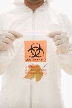 Man in biohazard suit and rubber gloves holding plastic biohazard bag containing orange Maple leaf.