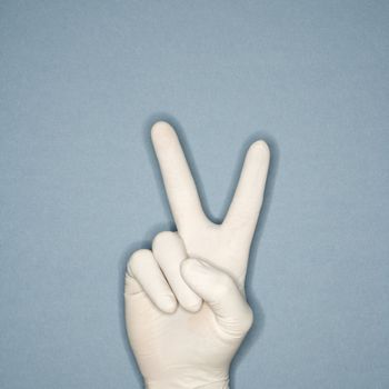 Hand wearing white rubber glove making a gesture meaning peace.