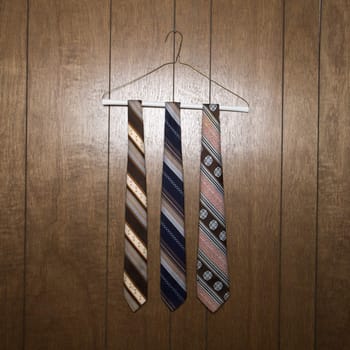 Three retro ties hanging on a wire hanger against wood paneling.