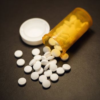 Open medicine bottle with pills spilling out onto table.