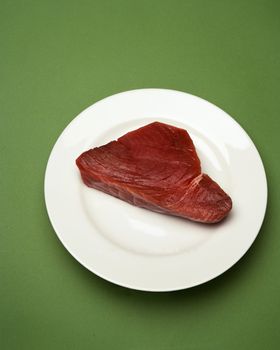 Raw tuna steak on white plate with green background
