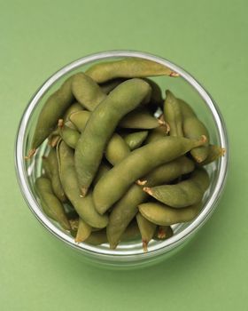 Fresh green soybean pods in glass bowl on green background
