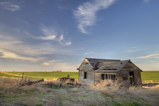 old abandoned house and farming machinery on Colorado prairie with green fields in background