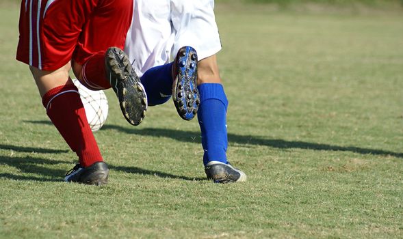 Two soccer players chasing a ball in a game running at the same speed.               