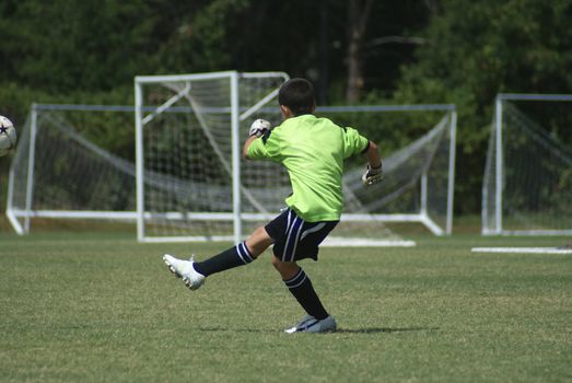 Soccer goalie kicking the ball in a game on a sunny day.                    