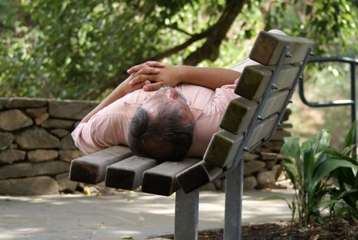 Man sleeping on a park bench during the day.              