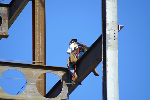 Man working on a skyscraper holding on to beam.                  