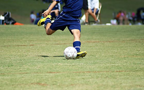 Young boy strking a soccer ball in a game wearing a blue uniform.              