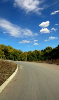 curved road uphill under blue sky with clouds