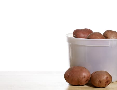 A pail of fresh organic garden red potatoes, shot on a wooden table with a solid white background
