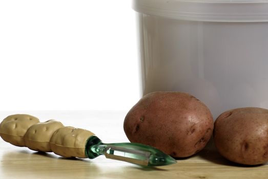 A potato peeler and organic red potatoes shot on a wooden table with a white background