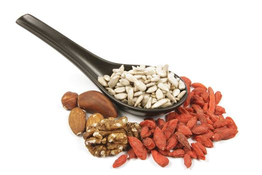 Sunflower seeds on a black spoon with mixed nuts and goji berries on a reflective white background