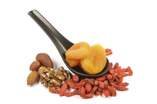 Dried juicy orange apricots on a spoon with mixed nuts and goji berries on a reflective white background