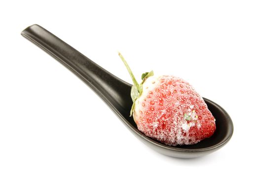 Red ripe frozen strawberry on a small black spoon with a reflective white background