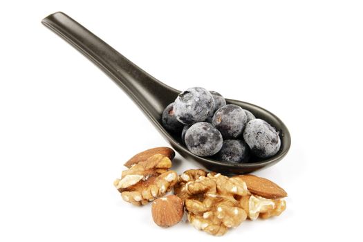Blue ripe blueberries on a small black spoon with mixed nuts on a reflective white background