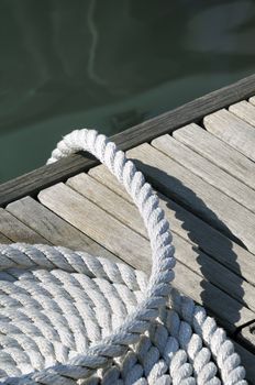 Close-up of a rolled-up rope on a wooden jetty with water in background