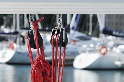 Close-up of sailing pulleys with red rope on a boom with boats of a marina in background